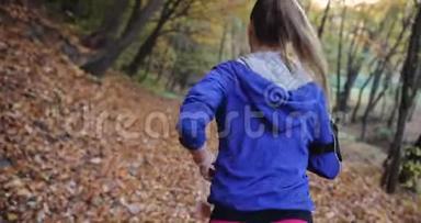 公园里的女跑步者。 穿着蓝色夹克和其他健身服的漂亮女人跑步时听音乐